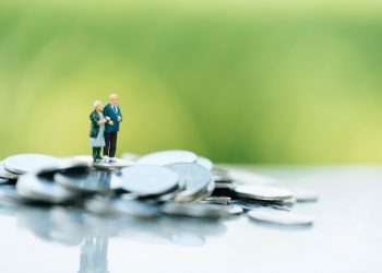 Concept of retirement planning. Miniature people: Old couple figure standing on top of coin stack.