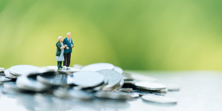 Concept of retirement planning. Miniature people: Old couple figure standing on top of coin stack.